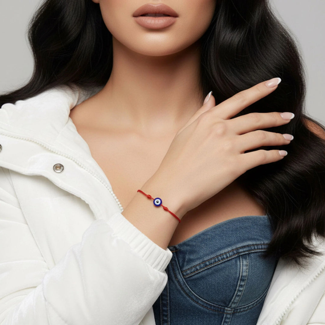 Woman wearing a red bracelet with a blue evil eye charm on a neutral background