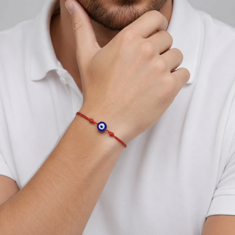 A close-up of a man's wrist wearing a red cord bracelet with a blue and white evil eye charm, paired with a white polo shirt.