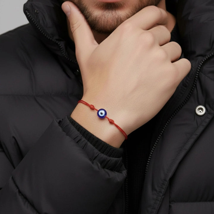Hand wearing a red string bracelet with an evil eye charm, against a dark background.