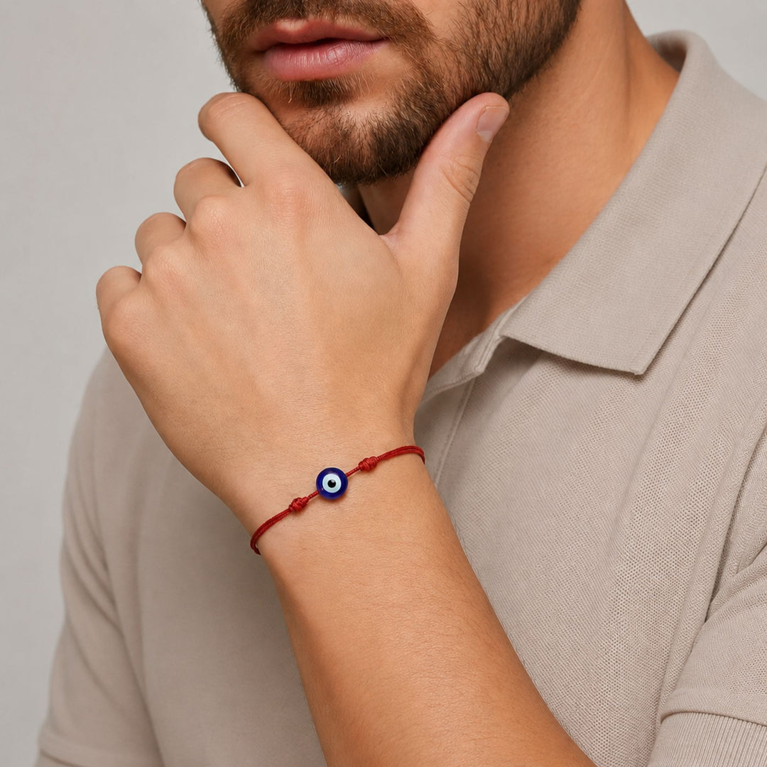 A close-up of a man wearing a red cord bracelet with a blue and white evil eye charm, paired with a beige polo shirt.
