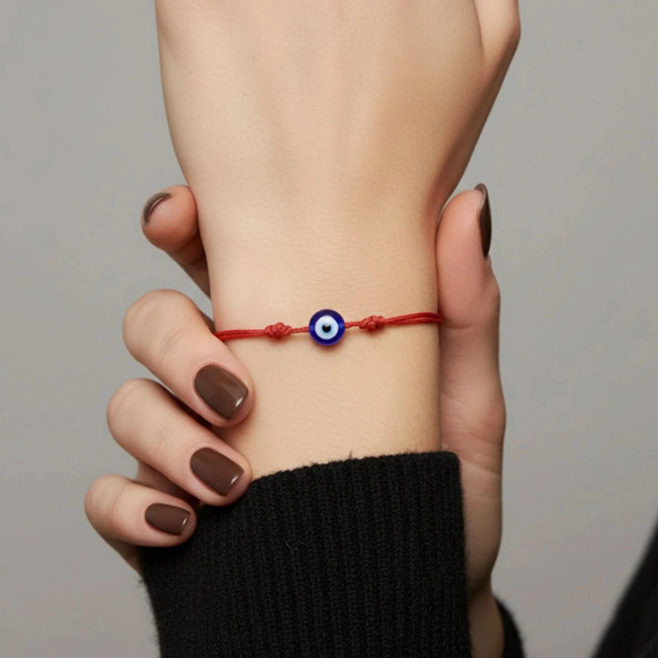 Hand wearing a red string bracelet with an evil eye charm on a neutral background