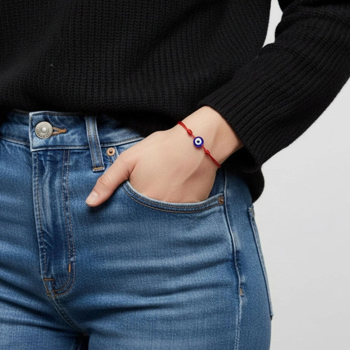Person wearing a red bracelet with a blue eye symbol on a plain background