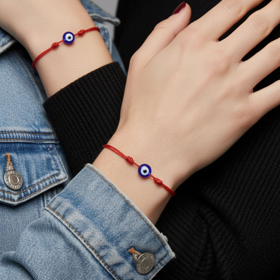 Close-up of a hand wearing a red string bracelet with a blue evil eye bead.
