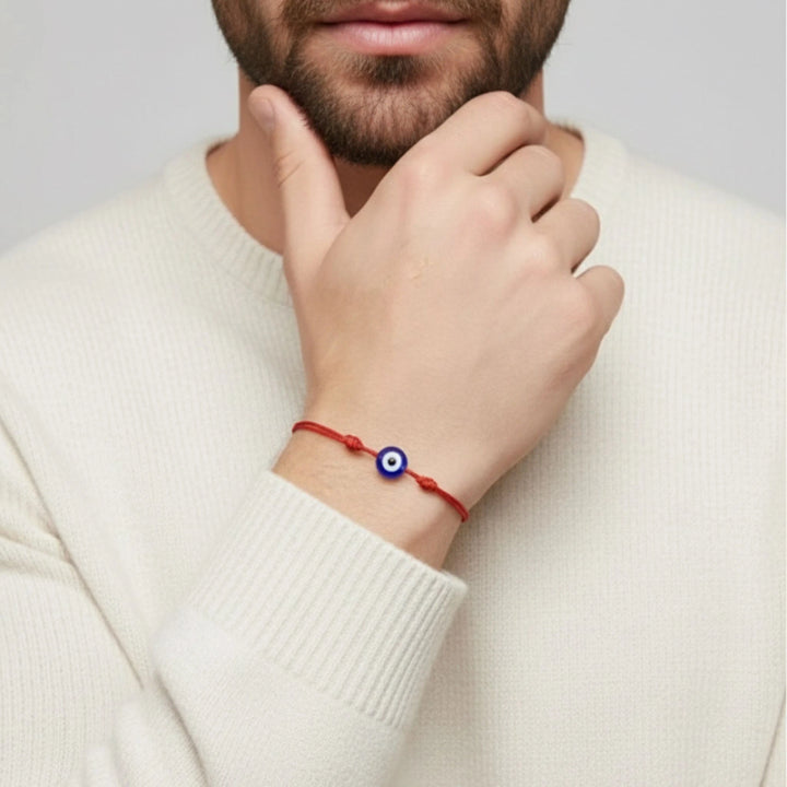 Person wearing a red bracelet with a blue evil eye charm on a plain background