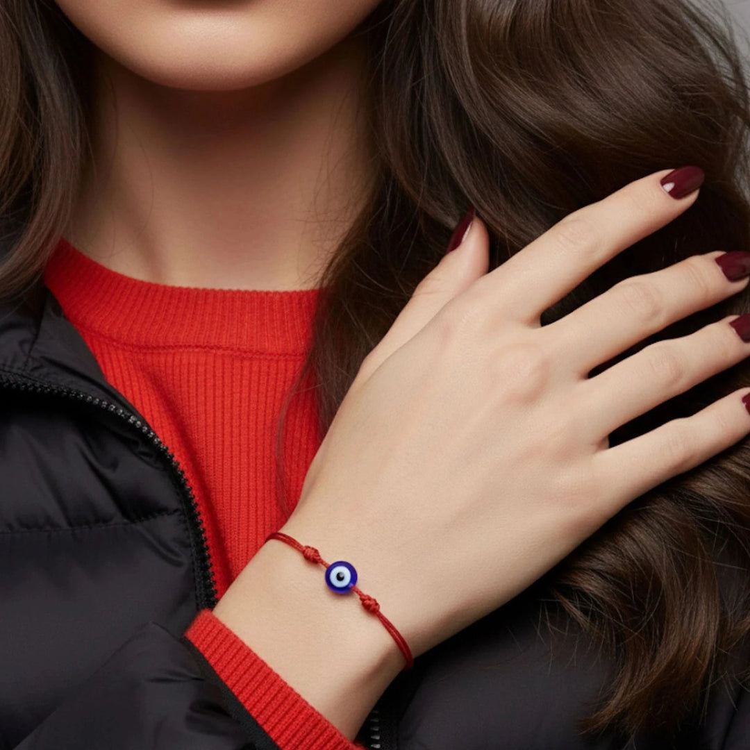 Person wearing a red bracelet with an evil eye charm, wearing a black jacket and red sweater.