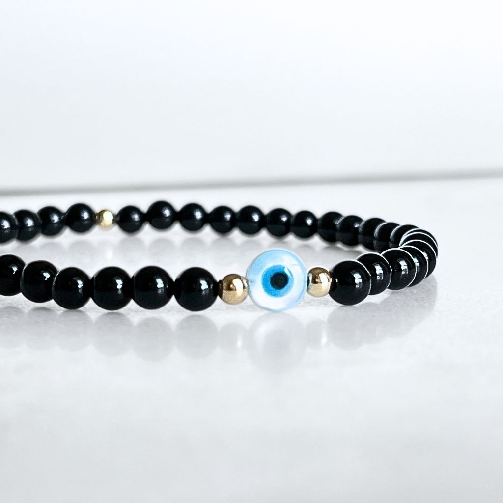 14K Gold and Black Tourmaline bracelet with Mother of Pearl evil eye on a wrist, highlighting the gold accents and snug fit - Luck Strings
