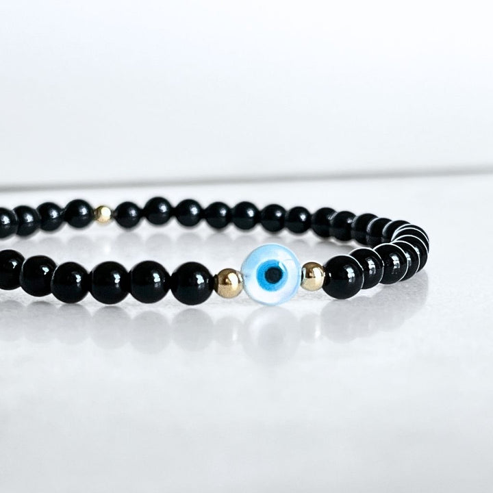 14K Gold and Black Tourmaline bracelet with Mother of Pearl evil eye on a wrist, highlighting the gold accents and snug fit - Luck Strings
