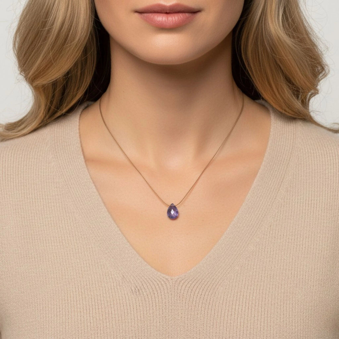 Woman wearing a necklace with a tanzanite teardrop pendant against a neutral background