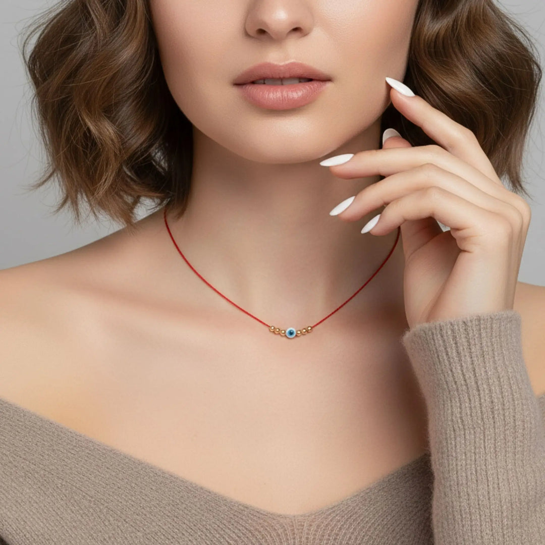 Woman wearing a red necklace with a evil eye blue pendant against a neutral background
