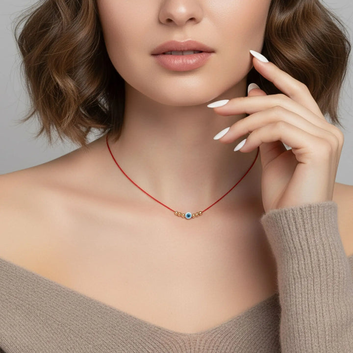 Woman wearing a red necklace with a evil eye blue pendant against a neutral background
