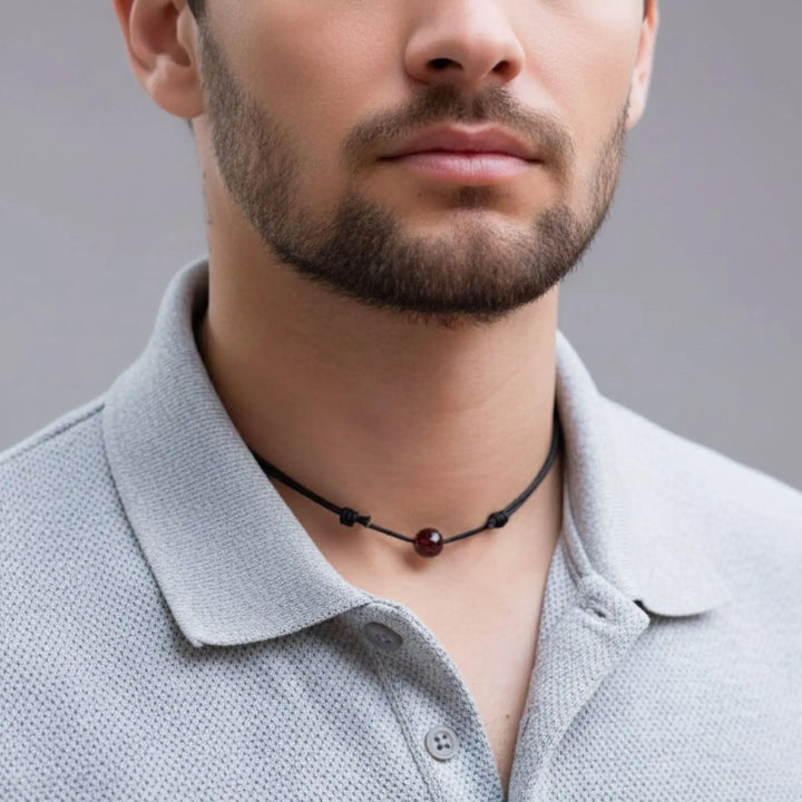 Man wearing a garnet necklace with a gray shirt against a neutral background