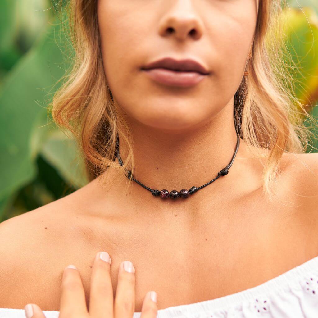 Close-up of a garnet choker adorning a woman's neck, with the deep red gemstones drawing attention, offered by Luck Strings.
