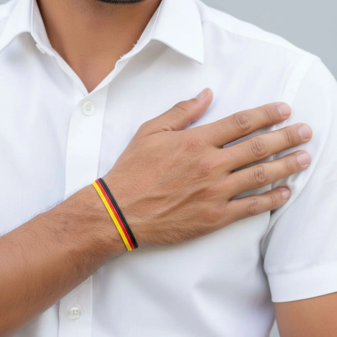 Person wearing a white shirt with a hand on chest and a Germany flag bracelet on wrist.