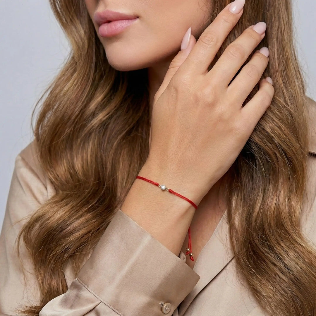 Close-up of a woman wearing a red bracelet with a small diamond, touching her hair against a neutral background.