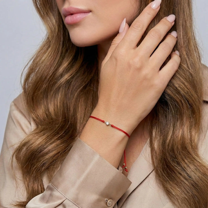 Close-up of a woman wearing a red bracelet with a small diamond, touching her hair against a neutral background.