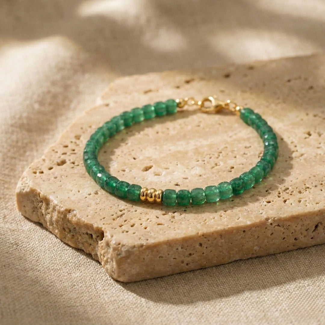 Green beaded bracelet with gold accents on a beige stone surface