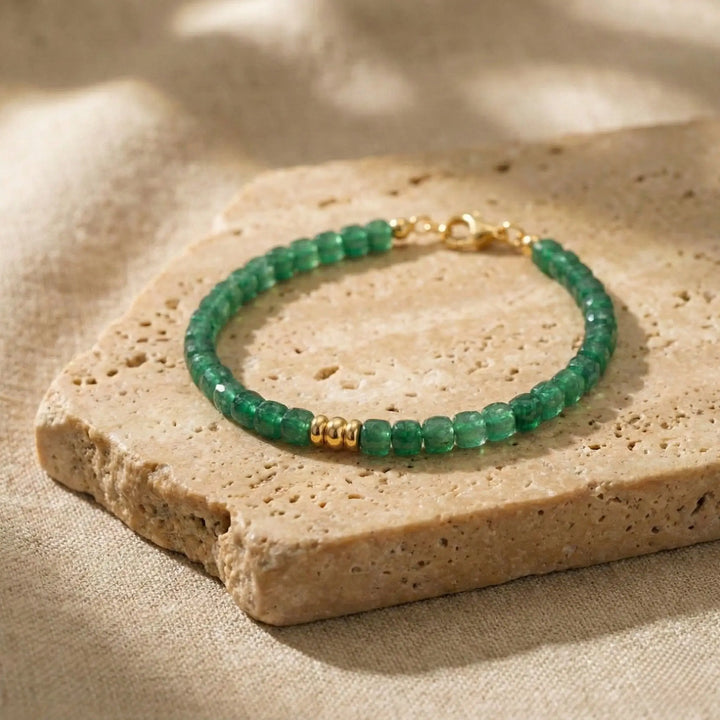 Green beaded bracelet with gold accents on a beige stone surface