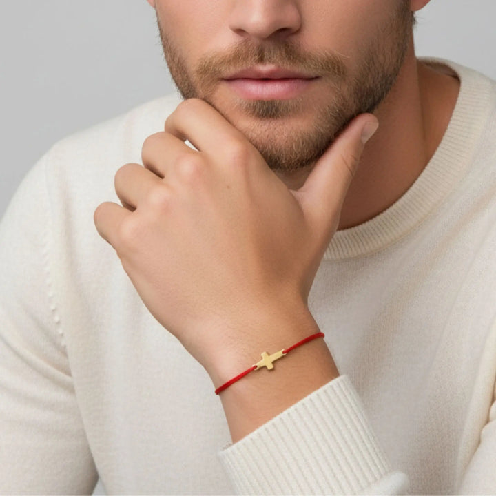 Man wearing a gold cross bracelet on a red cord, against a neutral background