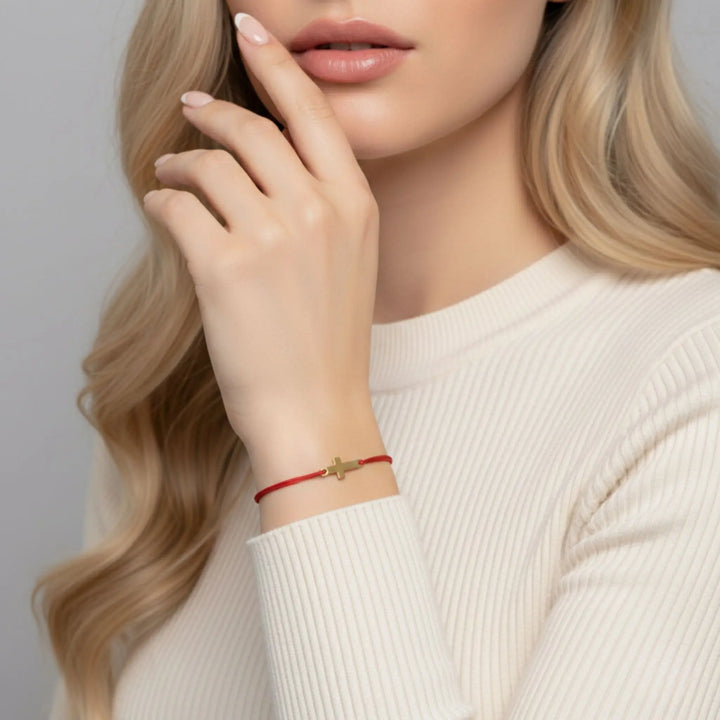 Woman wearing a red gold cross bracelet  on a neutral background