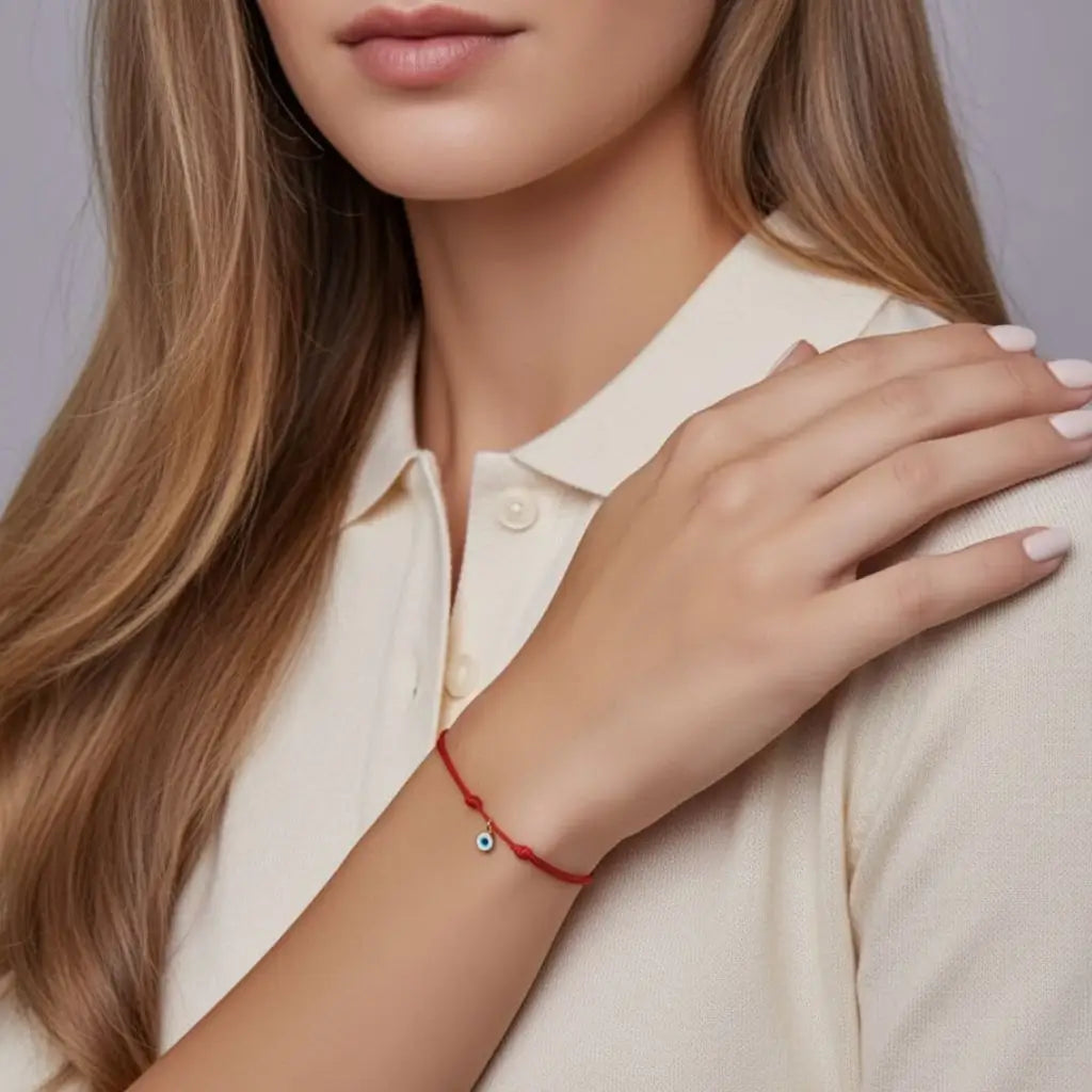 Woman wearing a red bracelet with a small gold evil eye charm, against a neutral background