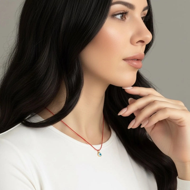 Woman wearing a red necklace with a small evil eye pendant against a neutral background