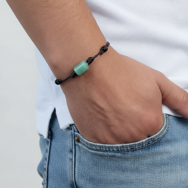 Green aventurine bracelet on black waxed cord, hand in pocket view.
