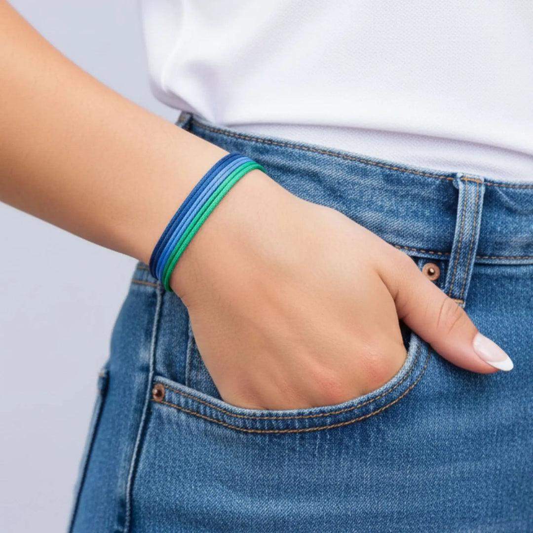 Hand with a blue bracelet in a pocket of blue jeans on a light gray background
