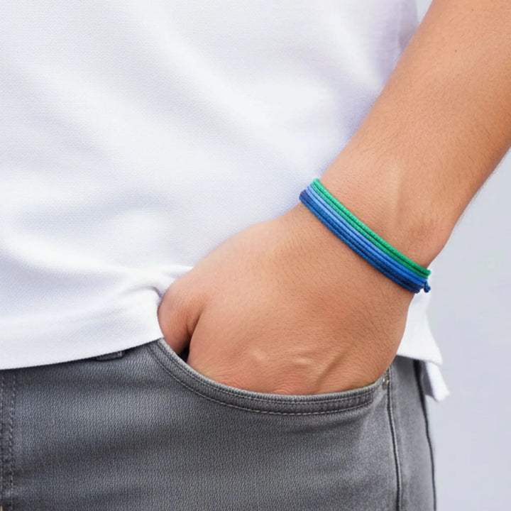 Person wearing a blue and green bracelet with a white shirt and gray pants.