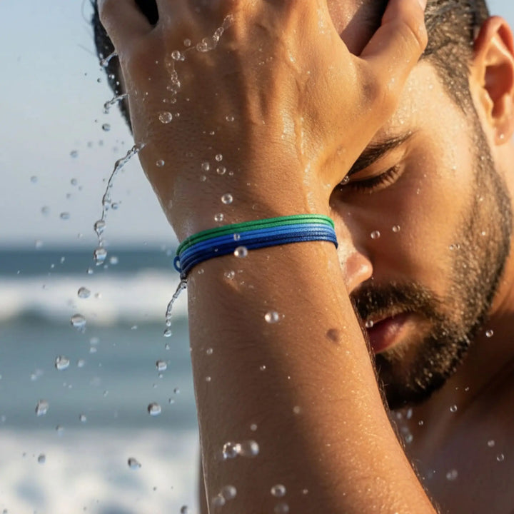 Man with a blue wristband shielding his face from water splashes outdoors