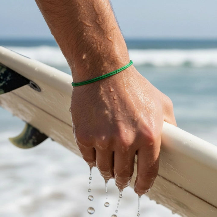 Hand holding a surfboard with water droplets, beach in the background
