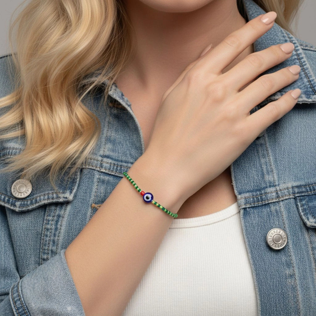 Person wearing a green bracelet with an evil eye symbol, wearing a denim jacket.
