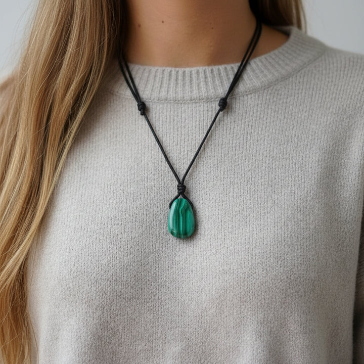 Person wearing a necklace with a green malachite pendant on a plain background