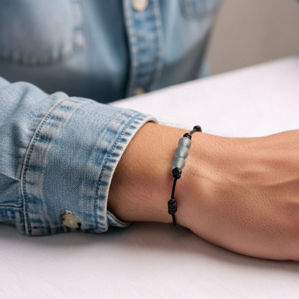 Person wearing a black beaded bracelet on a light surface with a denim sleeve.