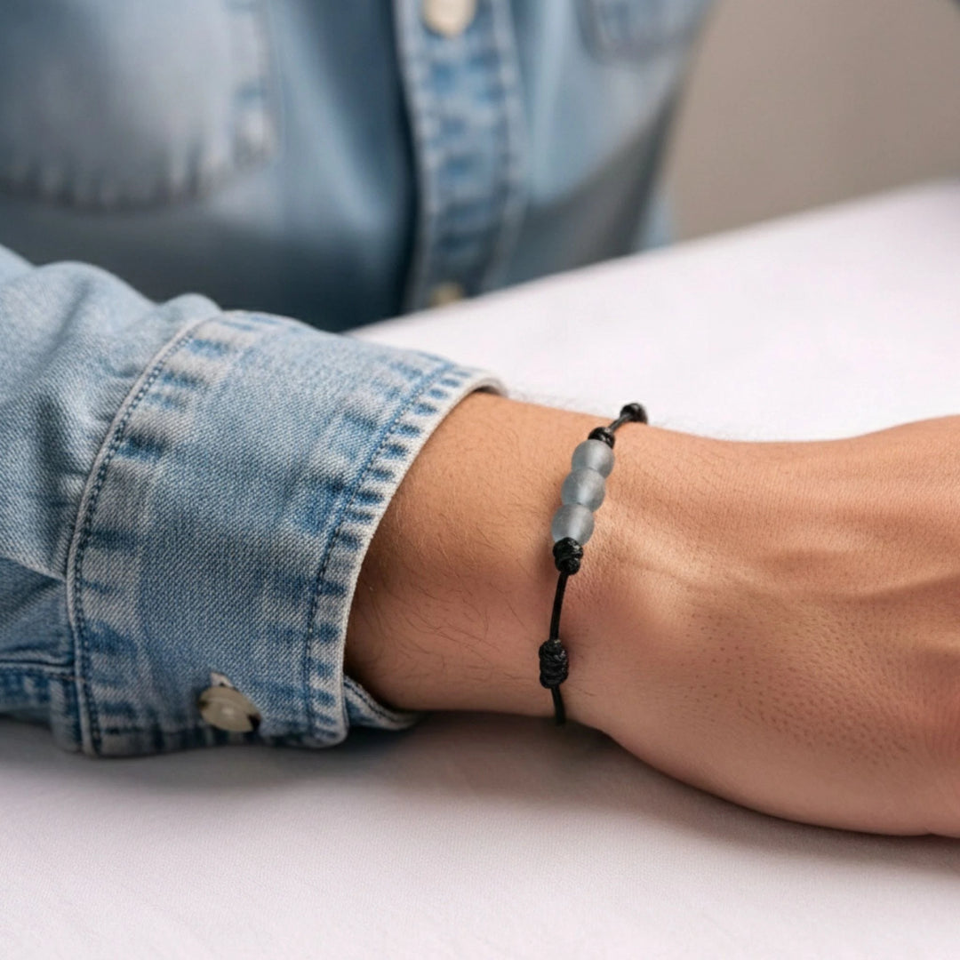 Person wearing a black beaded bracelet on a light surface with a denim sleeve.