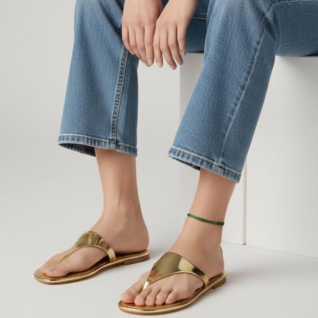 Gold sandals worn with blue jeans and green cord anklet on a white background