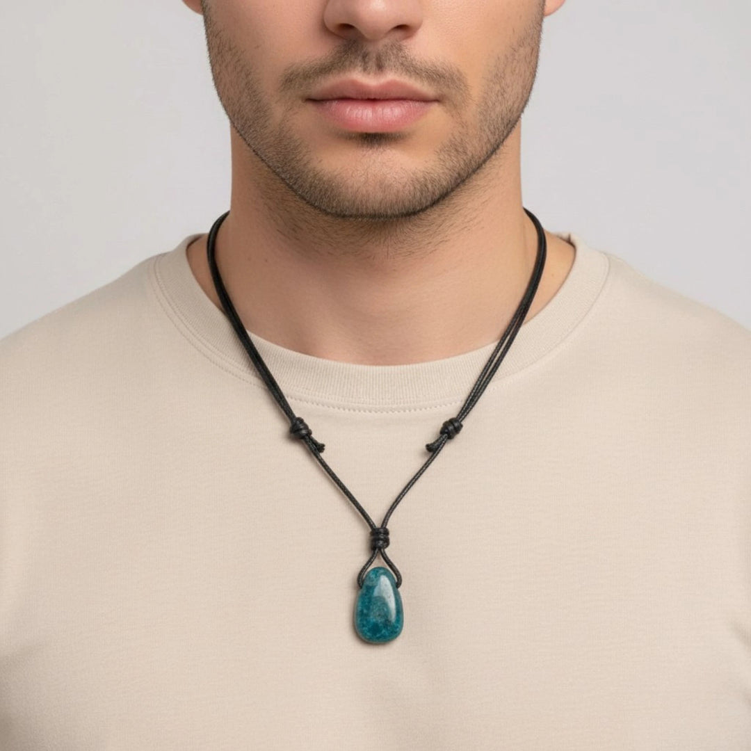 Man wearing a necklace with a blue Apatite pendant on a plain background