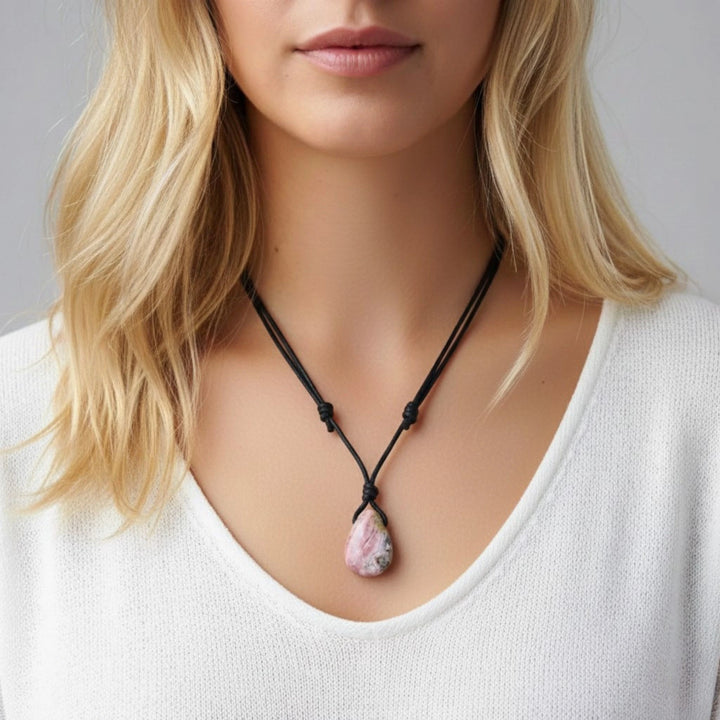 Woman wearing a necklace with a pink rhodochrosite pendant against a neutral background
