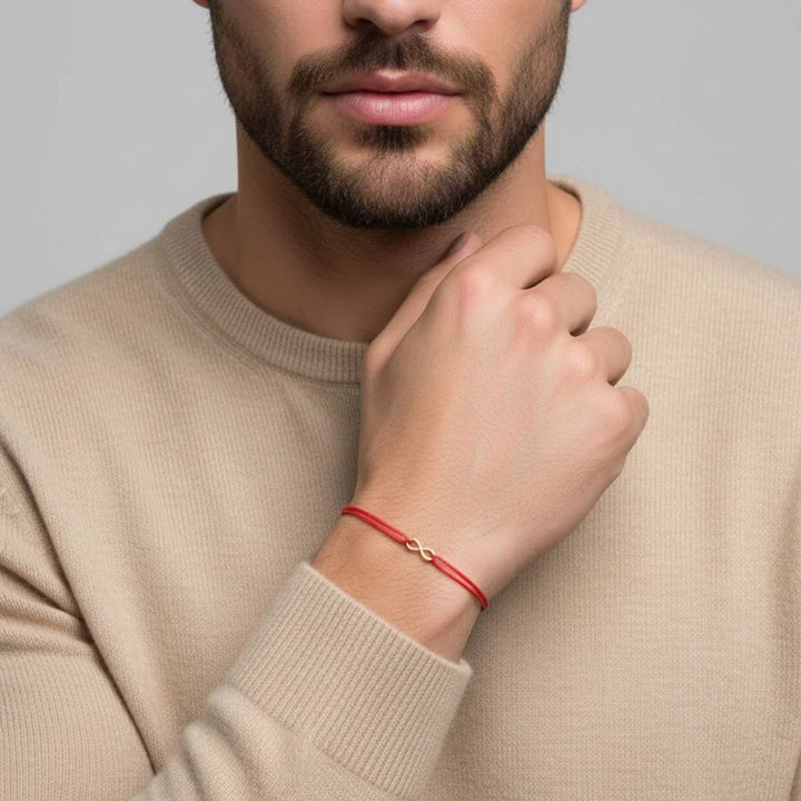 Man wearing a beige sweater with a red infinity bracelet on his wrist against a gray background