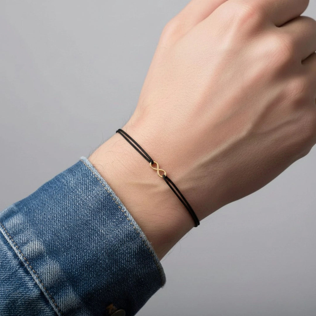 Hand wearing a black infinity bracelet with a gold heart charm on a gray background