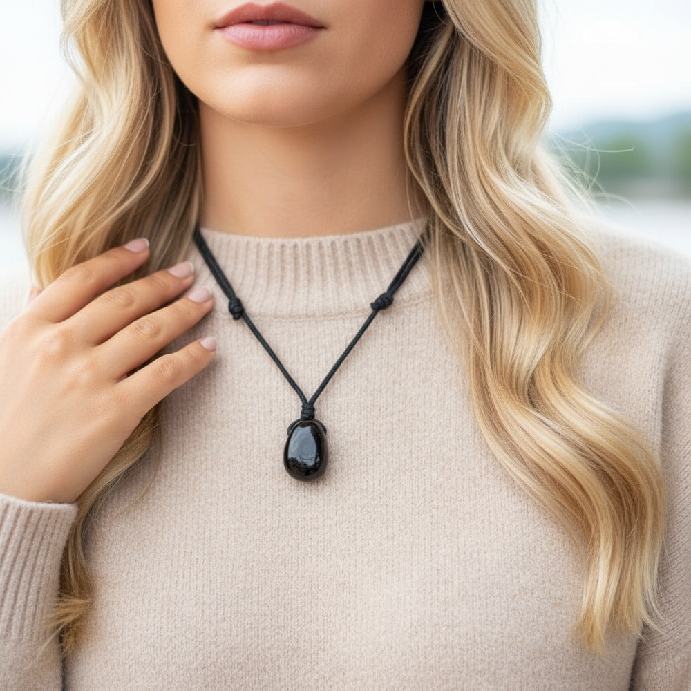 Woman wearing a jet black necklace with a dark pendant, holding it with her hand.