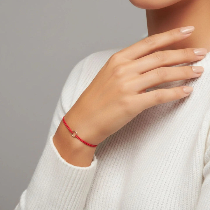 Hand wearing a red bracelet on a neutral background