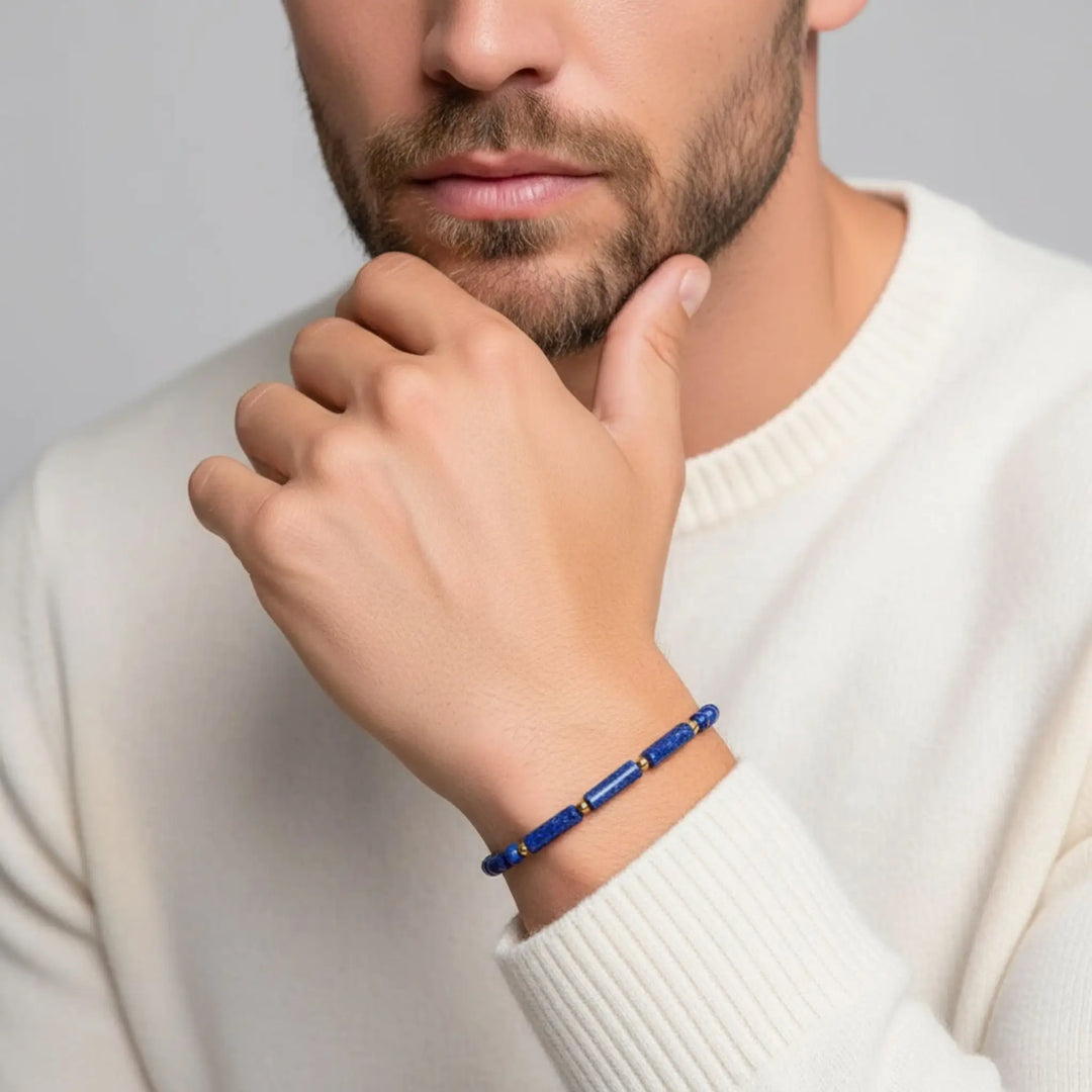 Man wearing a blue beaded bracelet on a plain background