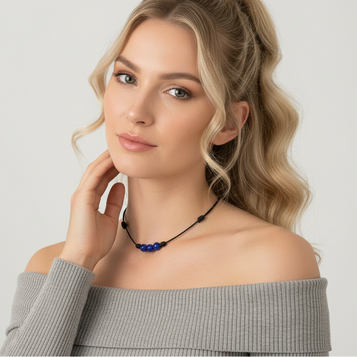 Woman wearing a gray off-shoulder top and a necklace with a lapis lazuli pendant on a light background