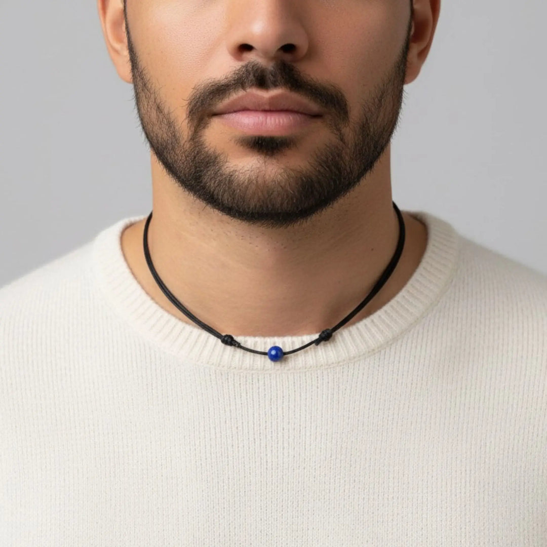 Man wearing a necklace with a blue lapis lazuli bead against a neutral background