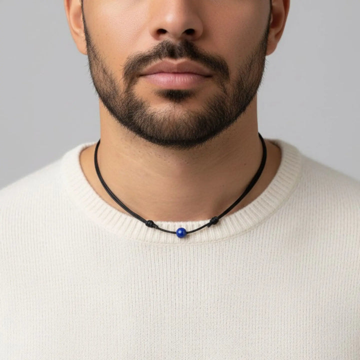 Man wearing a necklace with a blue lapis lazuli bead against a neutral background