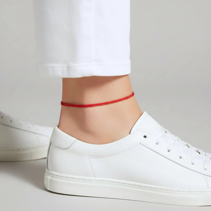 Red anklet on a person's ankle with white sneakers and pants.