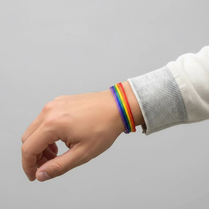Hand wearing a rainbow bracelet on a gray background