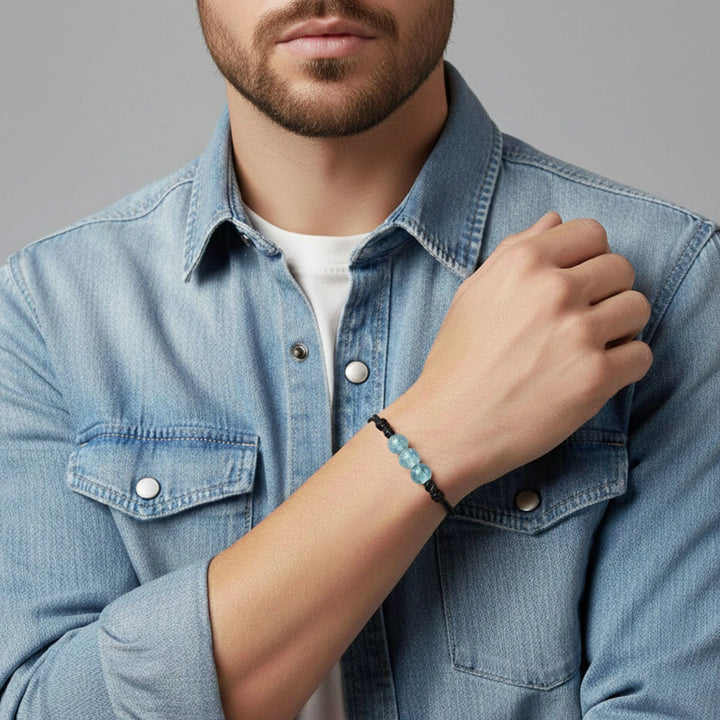 Man wearing a denim shirt with a glass bracelet on his wrist against a gray background