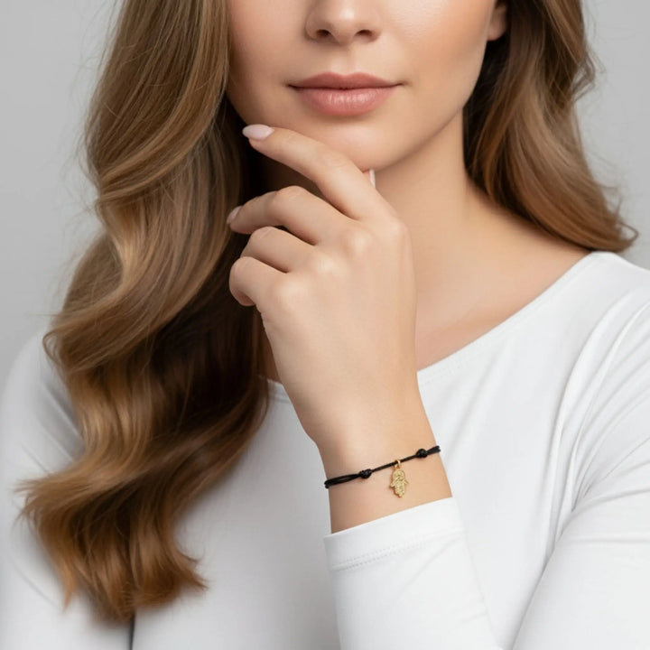 Woman wearing a black gold hamsa bracelet with a gold charm on a plain background