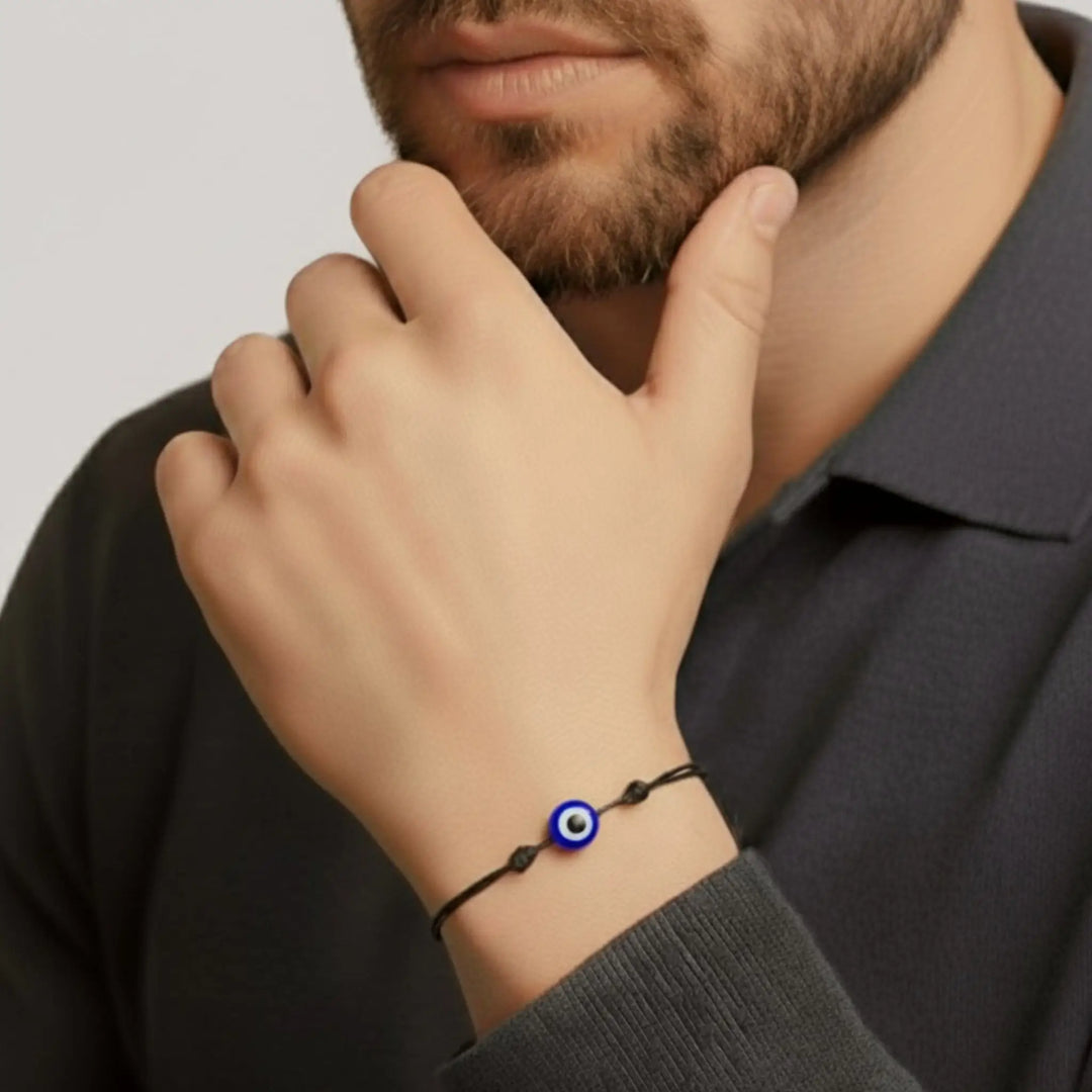 Person wearing a bracelet with an eye charm on a plain background